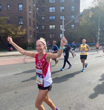NYC TCS Marathon SoleMate runs with arms above her head in celebration