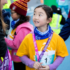 Girls on the Run participant smiling at volunteer handing out finisher medals at 5k